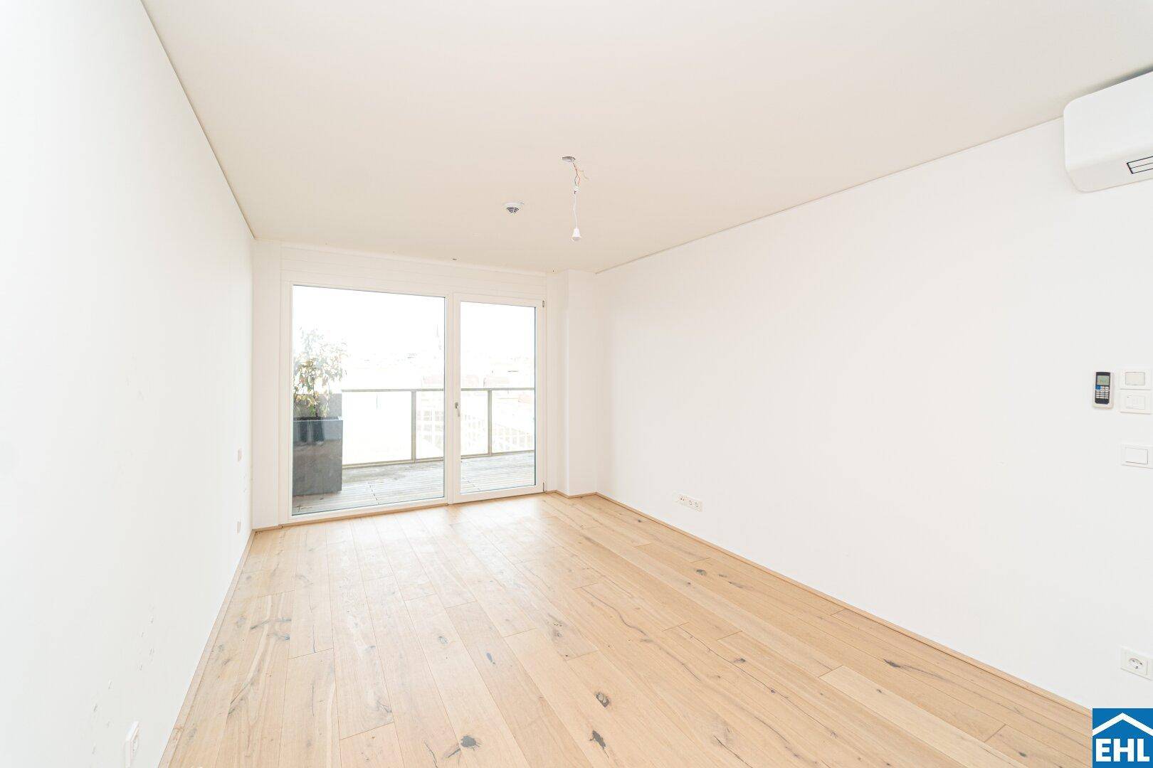 Helles Zimmer mit Holzboden, Klimaanlage und Zugang zu einem sonnigen Balkon.
