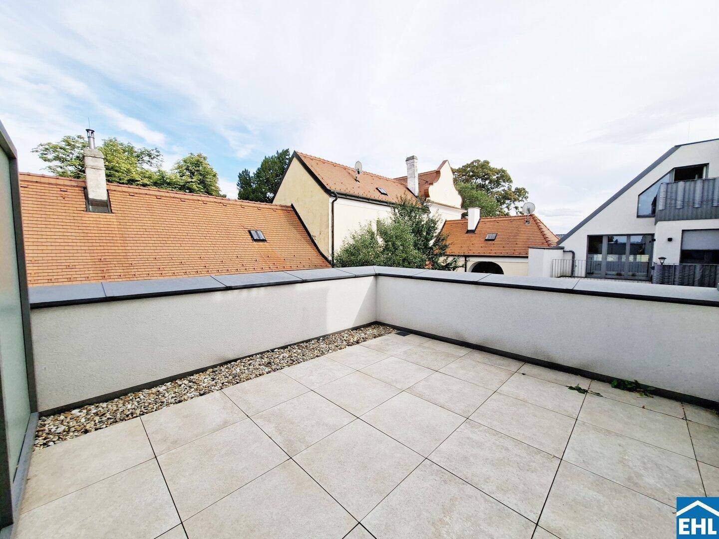 Helle Dachterrasse mit Blick auf traditionelle Dächer und den Himmel, umgeben von einer niedrigen Mauer.