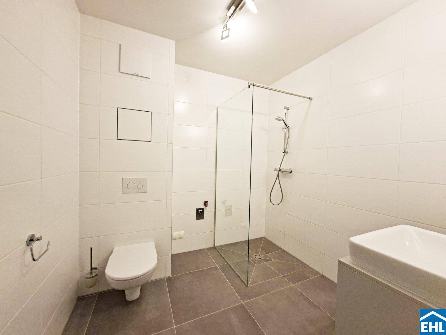 Modernes Badezimmer mit weißen Fliesen, ebenerdiger Dusche und wandhängendem WC.