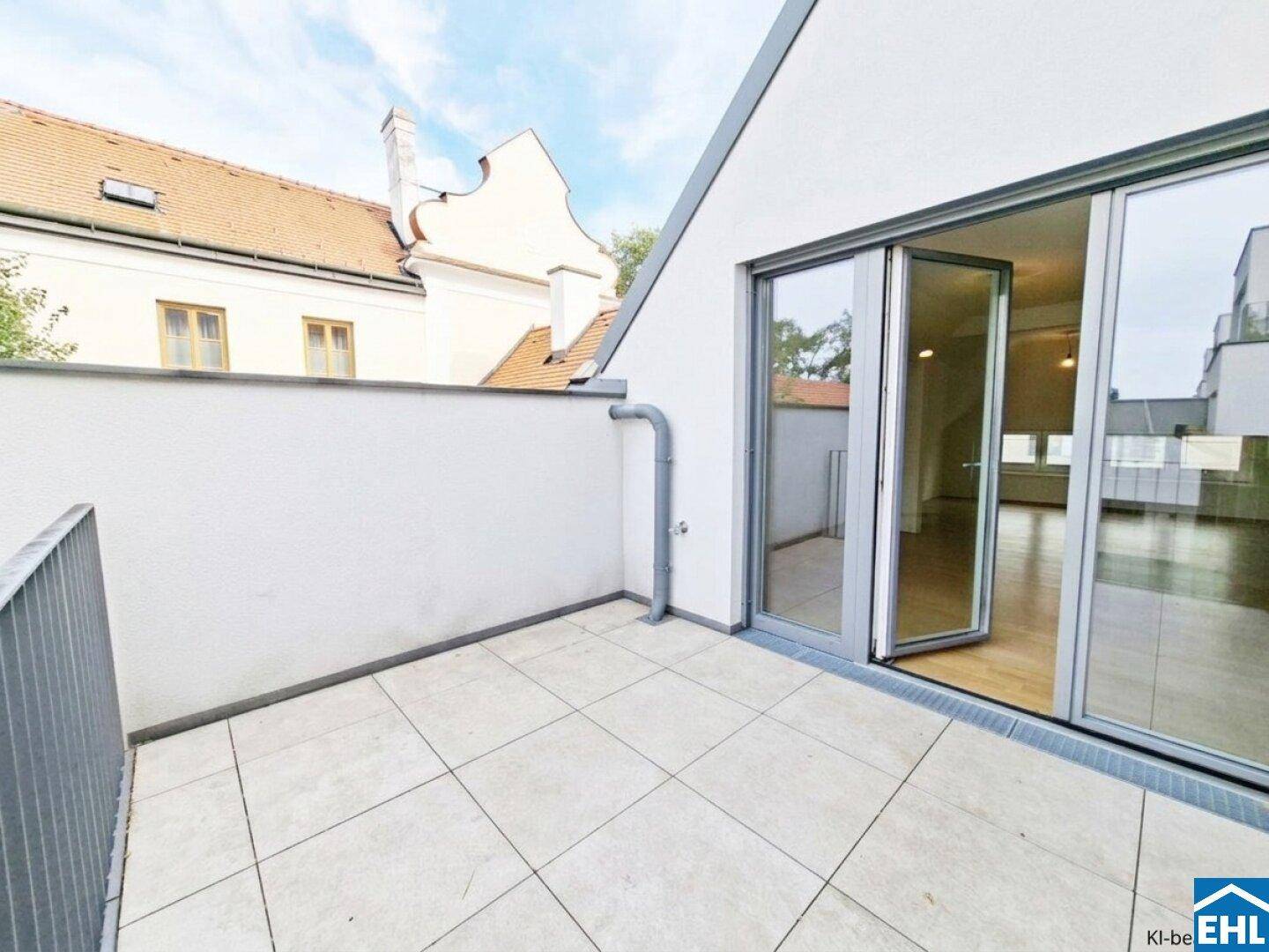 Heller Balkon mit Fliesenboden und Zugang zu einem lichtdurchfluteten Innenraum.
