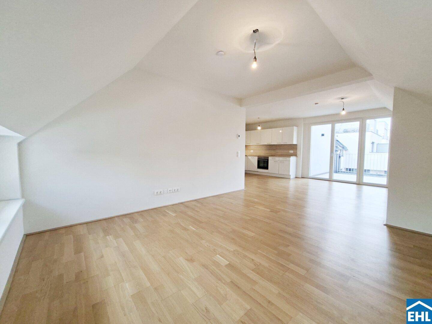 Weitläufiger, offener Wohnbereich mit hellem Parkettboden und Zugang zum Balkon.