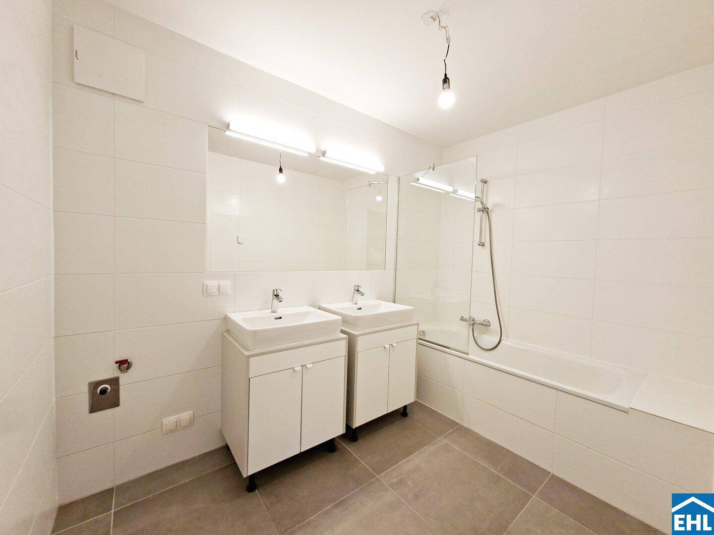 Modernes Badezimmer mit Doppelwaschbecken, Badewanne und weißen Fliesen.