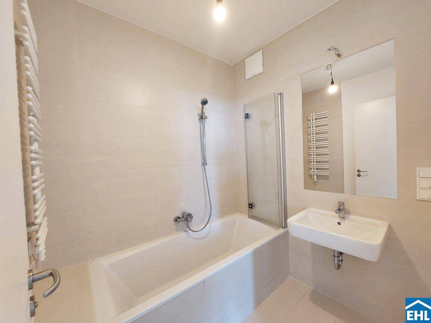 Modernes Badezimmer mit Badewanne, Duschabtrennung aus Glas, Einzelwaschbecken und beheiztem Handtuchhalter.
