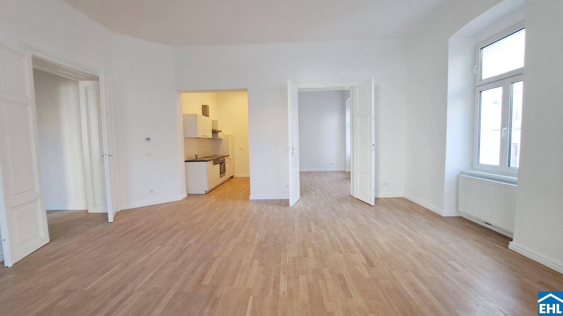 Geräumiges Zimmer mit Parkettboden und Zugang zu einer kleinen Küche sowie weiteren Räumen.