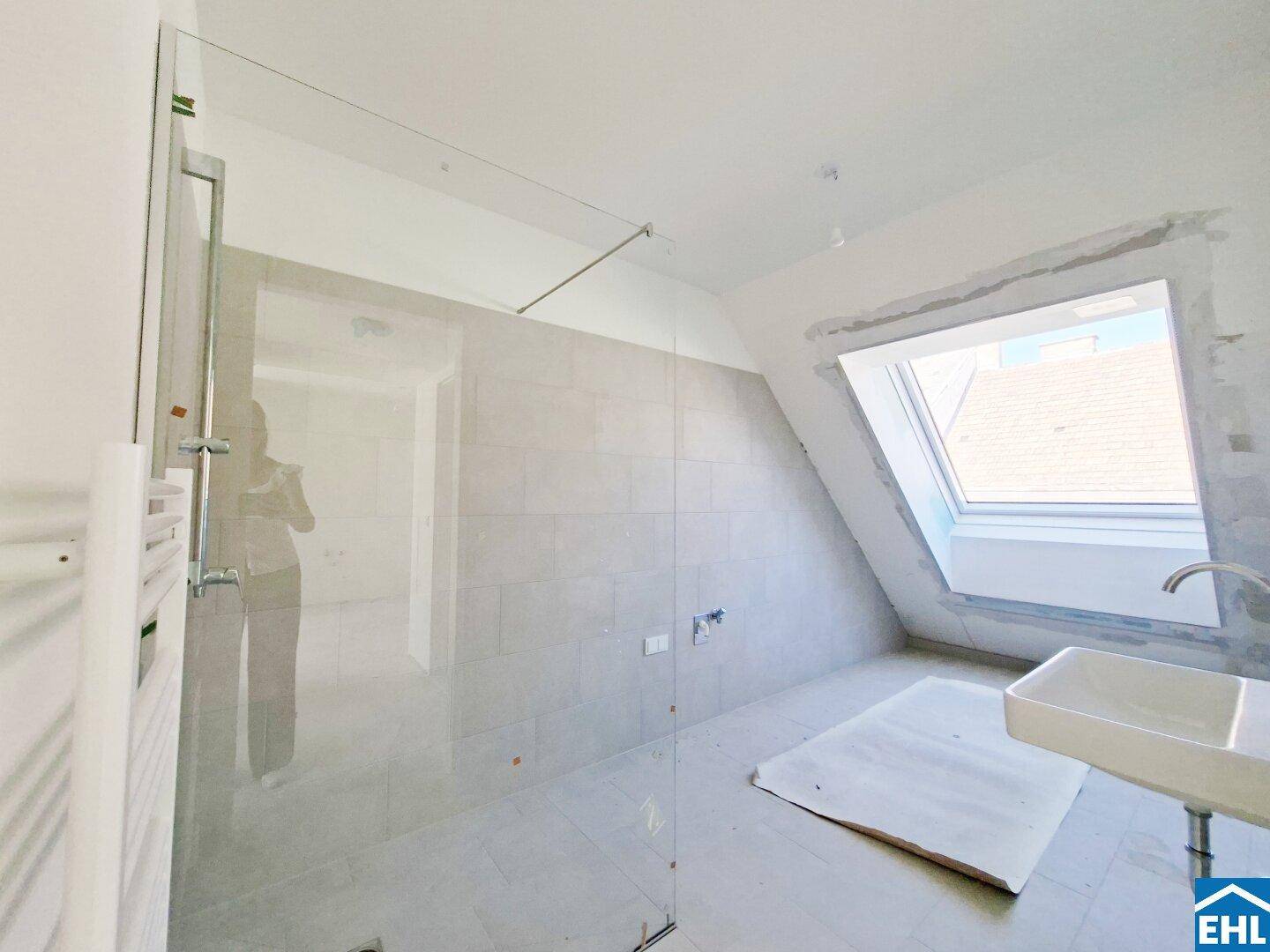 Modernes Badezimmer im Rohbau mit begehbarer Dusche, Waschbecken und Dachfenster.