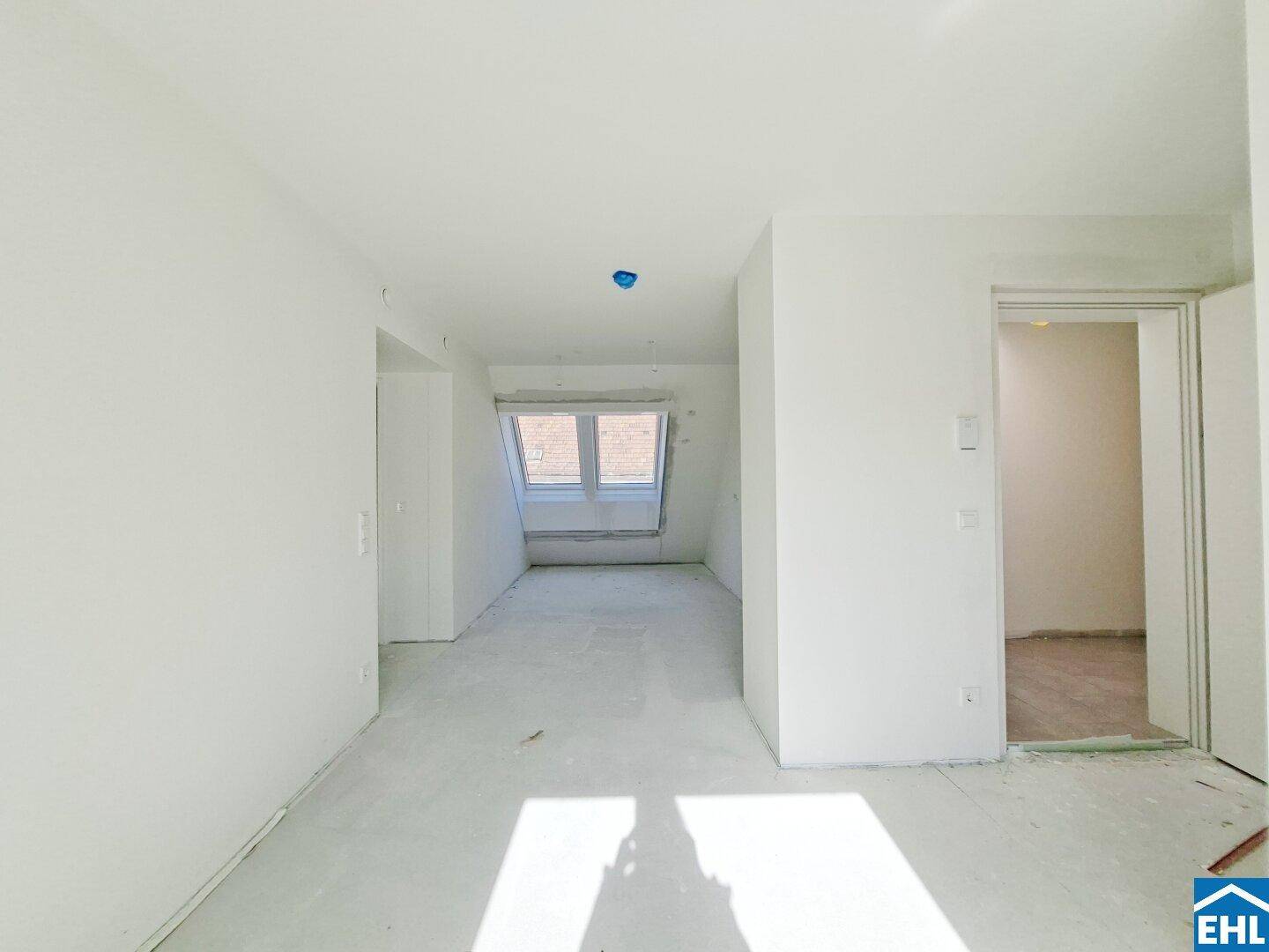Heller, unmöblierter Raum im Rohbau mit schrägem Dachfenster und viel Tageslicht.