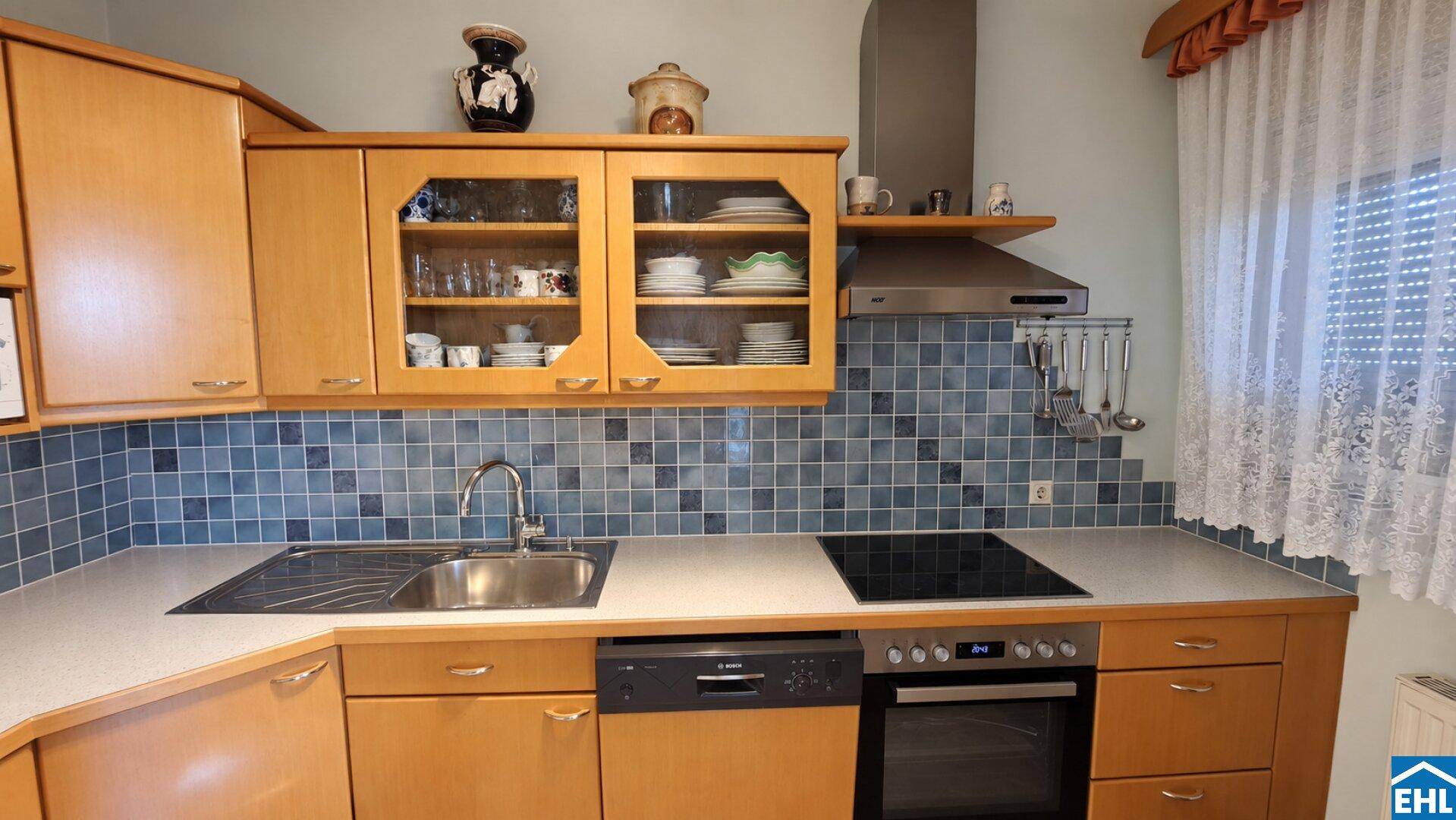 Funktionale Küche mit Holzschränken, blauen Fliesen und integrierten modernen Küchengeräten.
