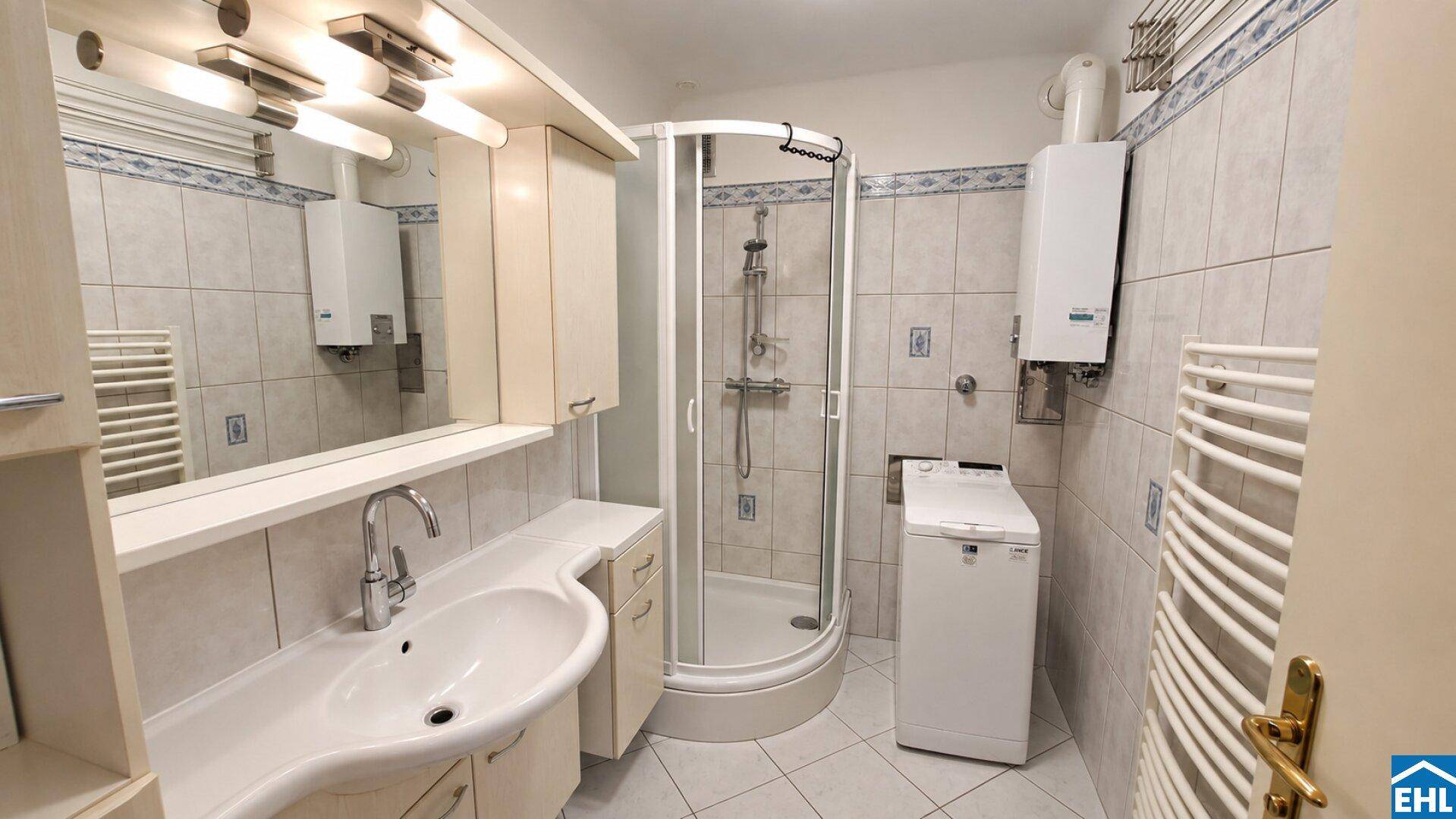 Helles Badezimmer mit Duschkabine, Einzelwaschbecken, Handtuchheizkörper und Waschmaschine.