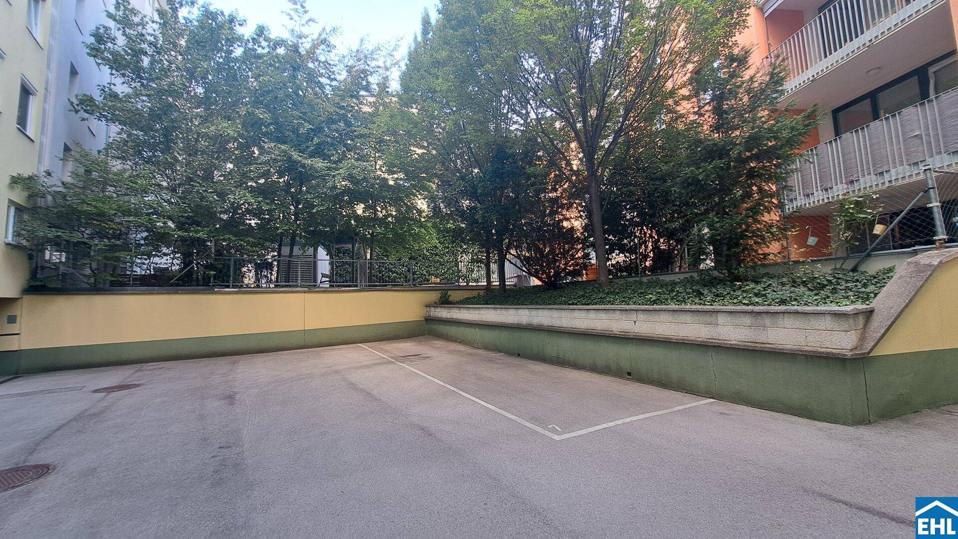 Außenparkplatz mit Baumbestand und Begrenzungsmauern, bietet Stellfläche für Fahrzeuge.