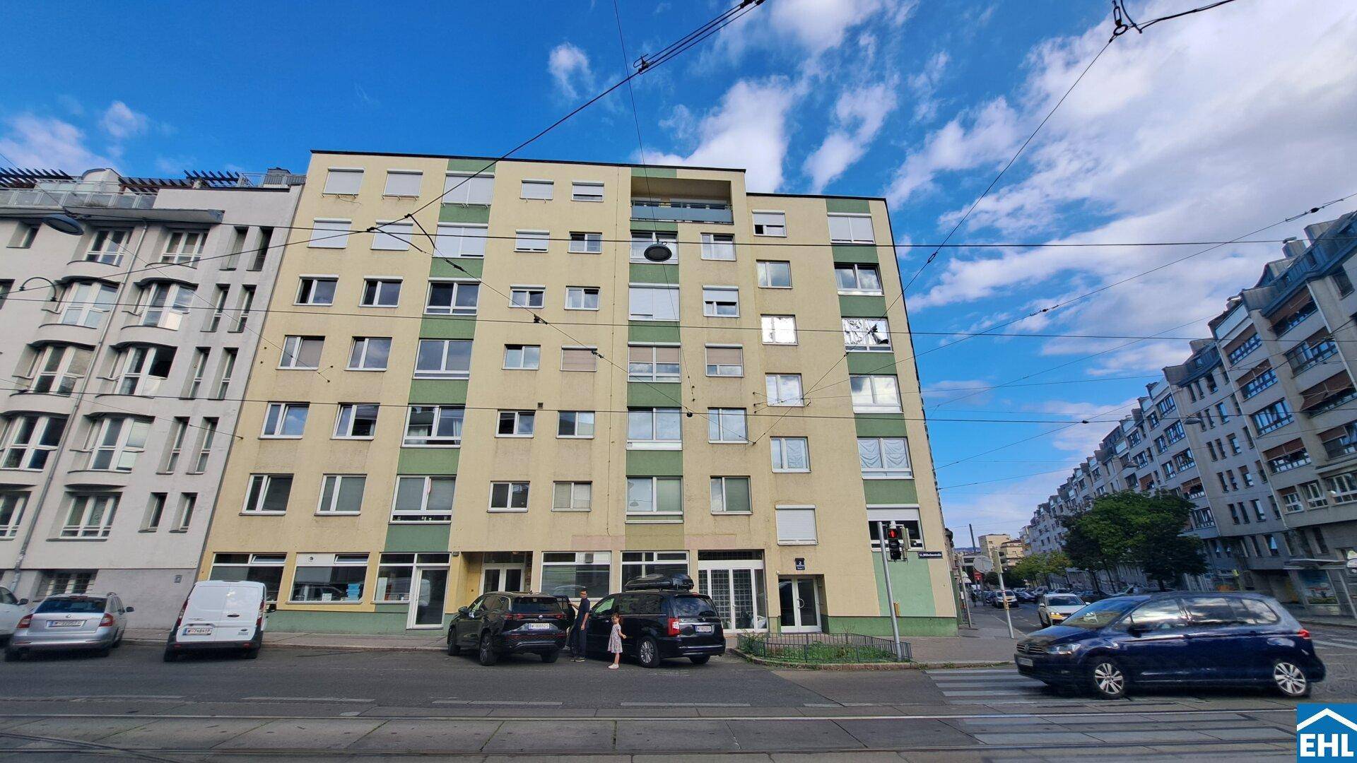Mehrstöckiges Wohngebäude an einer belebten Straße mit Geschäften im Erdgeschoss.