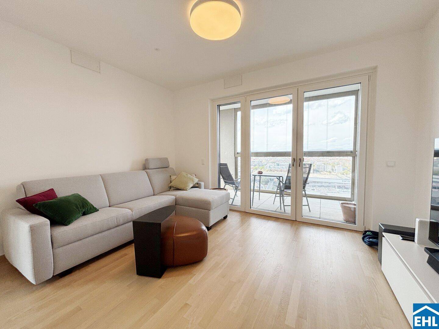 Gemütliches Wohnzimmer mit L-förmigem Sofa und Zugang zu einem Außenbereich mit Stadtblick.