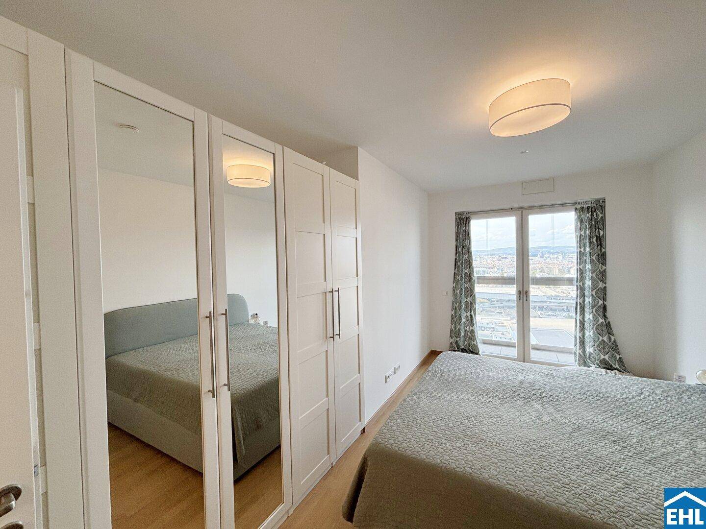 Schlafzimmer mit großem Bett, Spiegelschränken und Fenster mit Blick auf die Stadt.