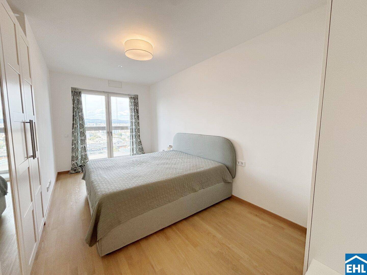Helles Schlafzimmer mit Doppelbett und großem Fenster, das viel Tageslicht hereinlässt.