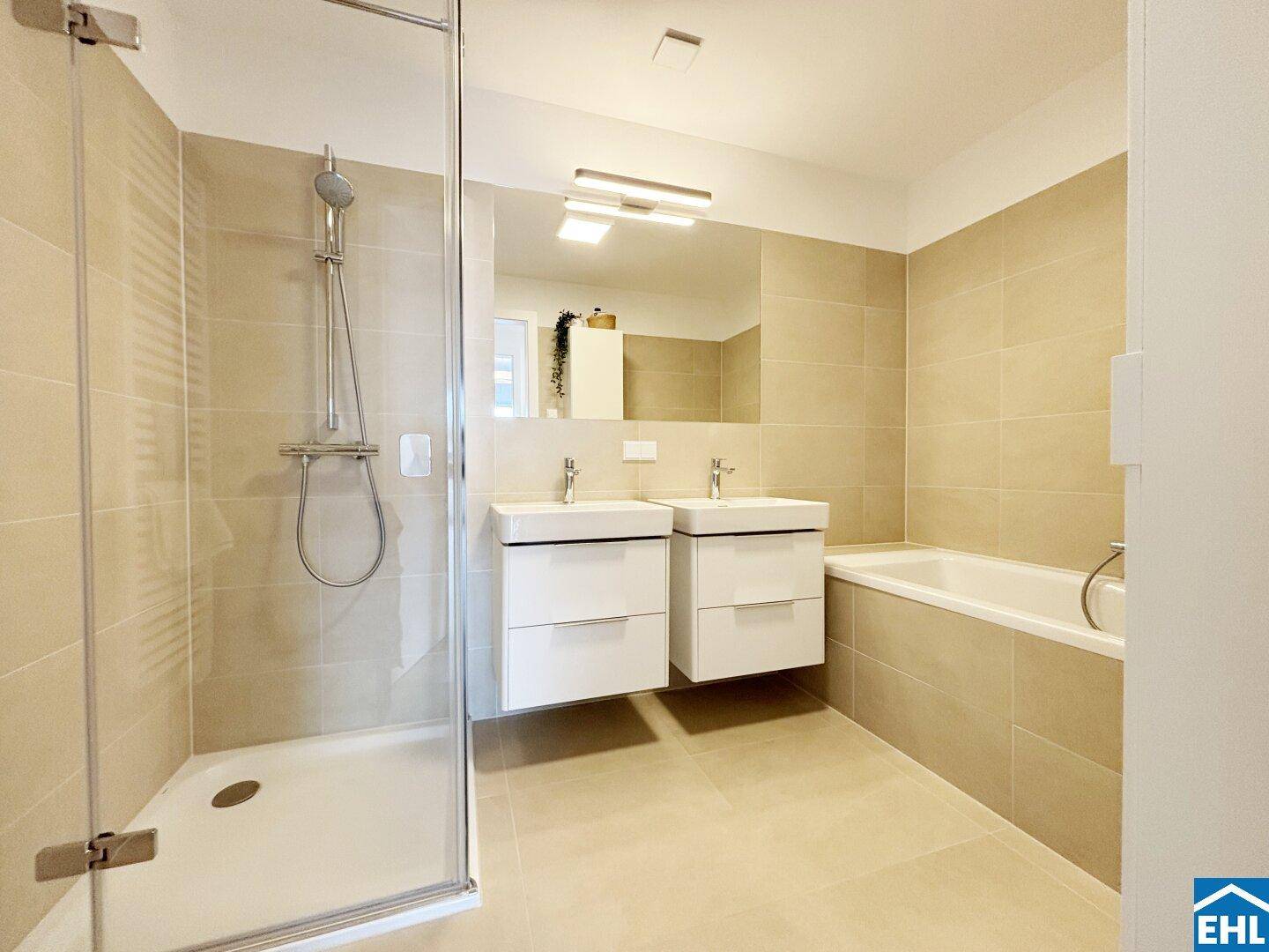Modernes Badezimmer mit beigen Fliesen, Doppelwaschbecken, Dusche und Badewanne.