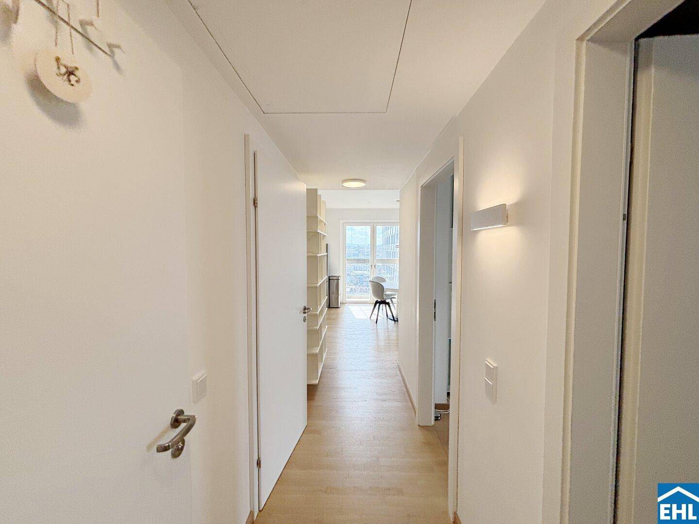 Heller Flur mit Holzboden und weiß gestrichenen Wänden, der zu den Wohnbereichen führt.