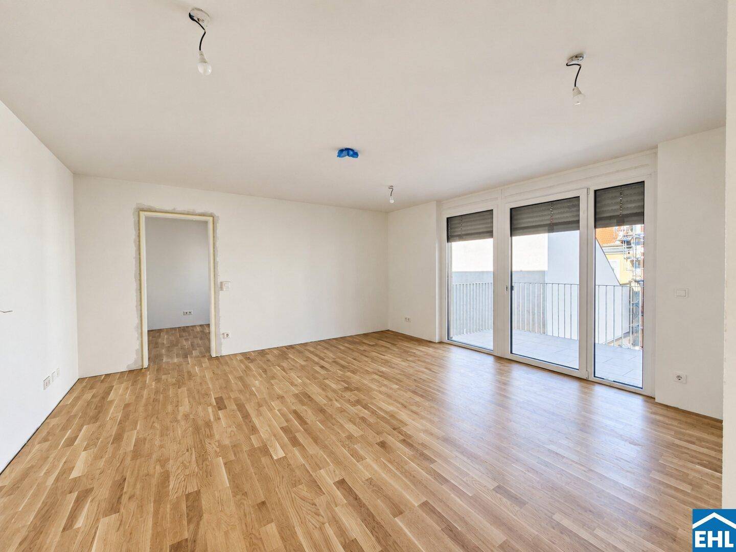 Geräumiges Wohnzimmer mit Holzboden und großen Fenstern, die viel Tageslicht hereinlassen.