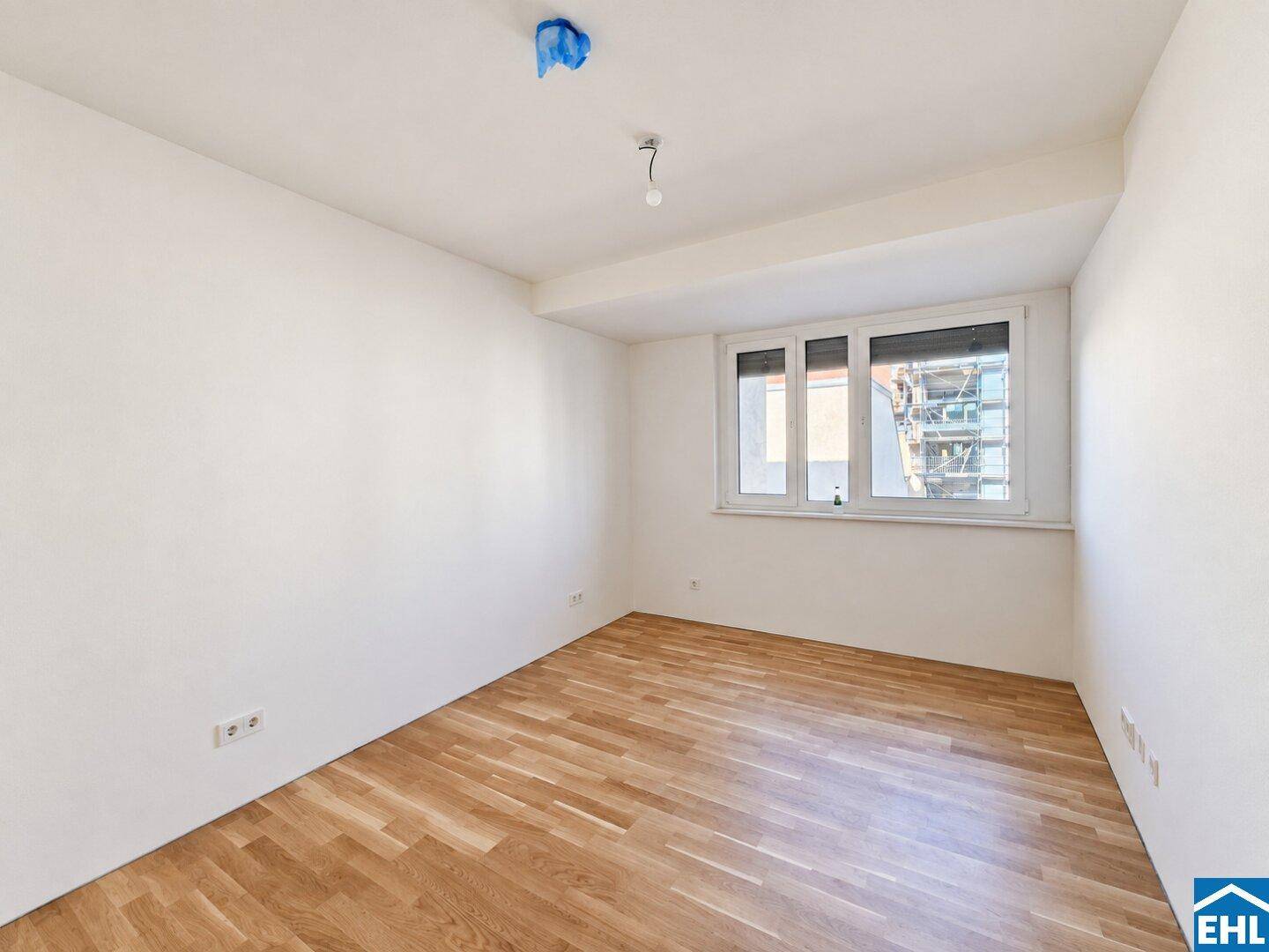 Leeres Schlafzimmer mit Parkettboden und einem Fenster, das den Blick nach draußen freigibt.