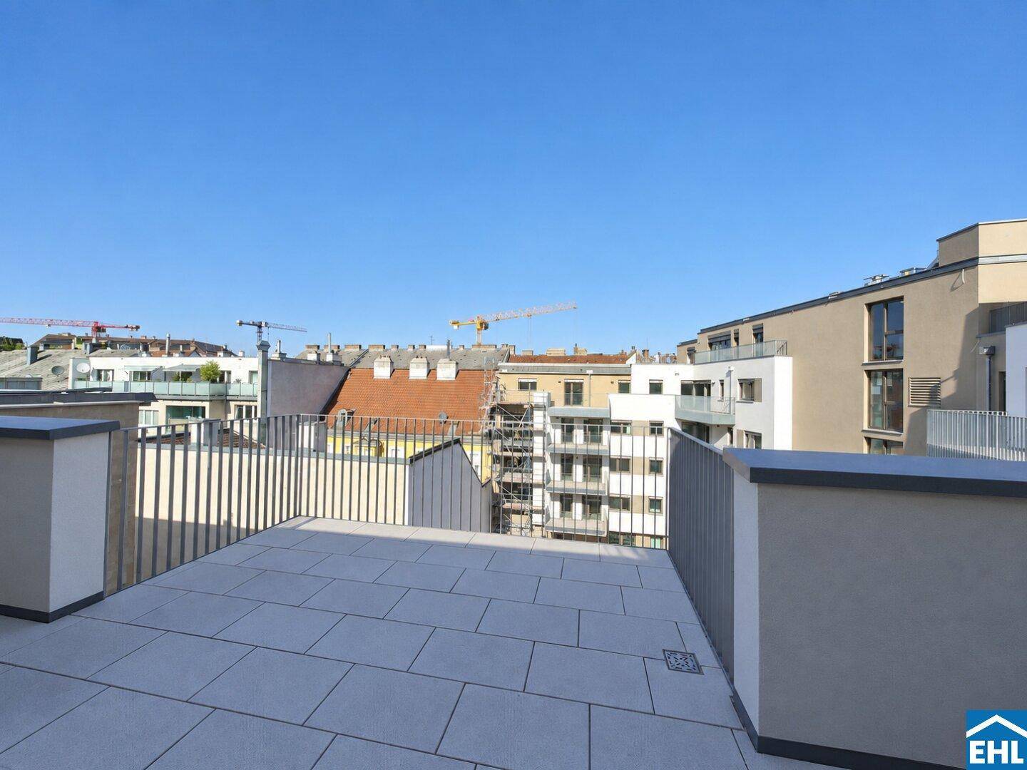 Geräumige Dachterrasse mit Fliesenboden und Blick über die Stadt und umliegende Gebäude.