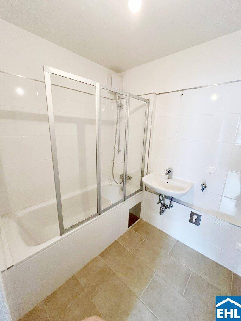 Badezimmer mit Badewanne, Duschabtrennung, Waschbecken und hellen Fliesen.