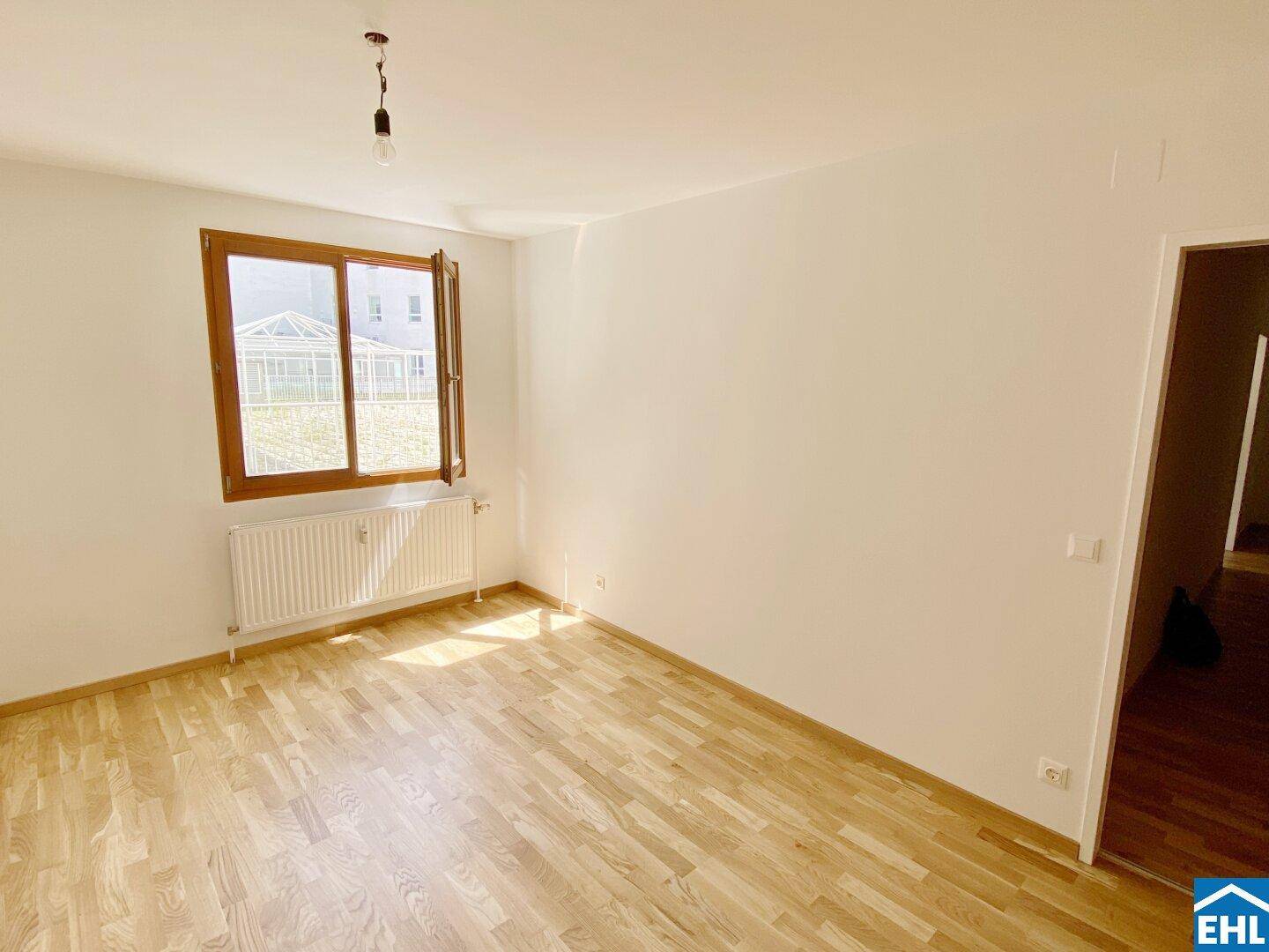 Ruhiges Zimmer mit Parkettboden, weißen Wänden und Blick auf eine angrenzende Struktur.