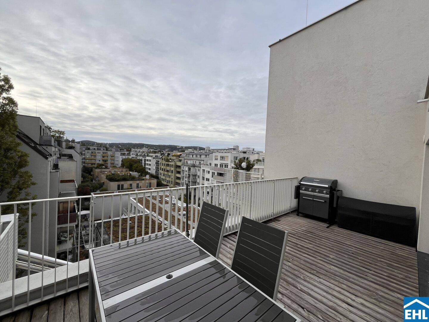Möblierte Terrasse mit Holzboden, Esstisch und Grill, bietet einen weiten Blick über die Stadt.