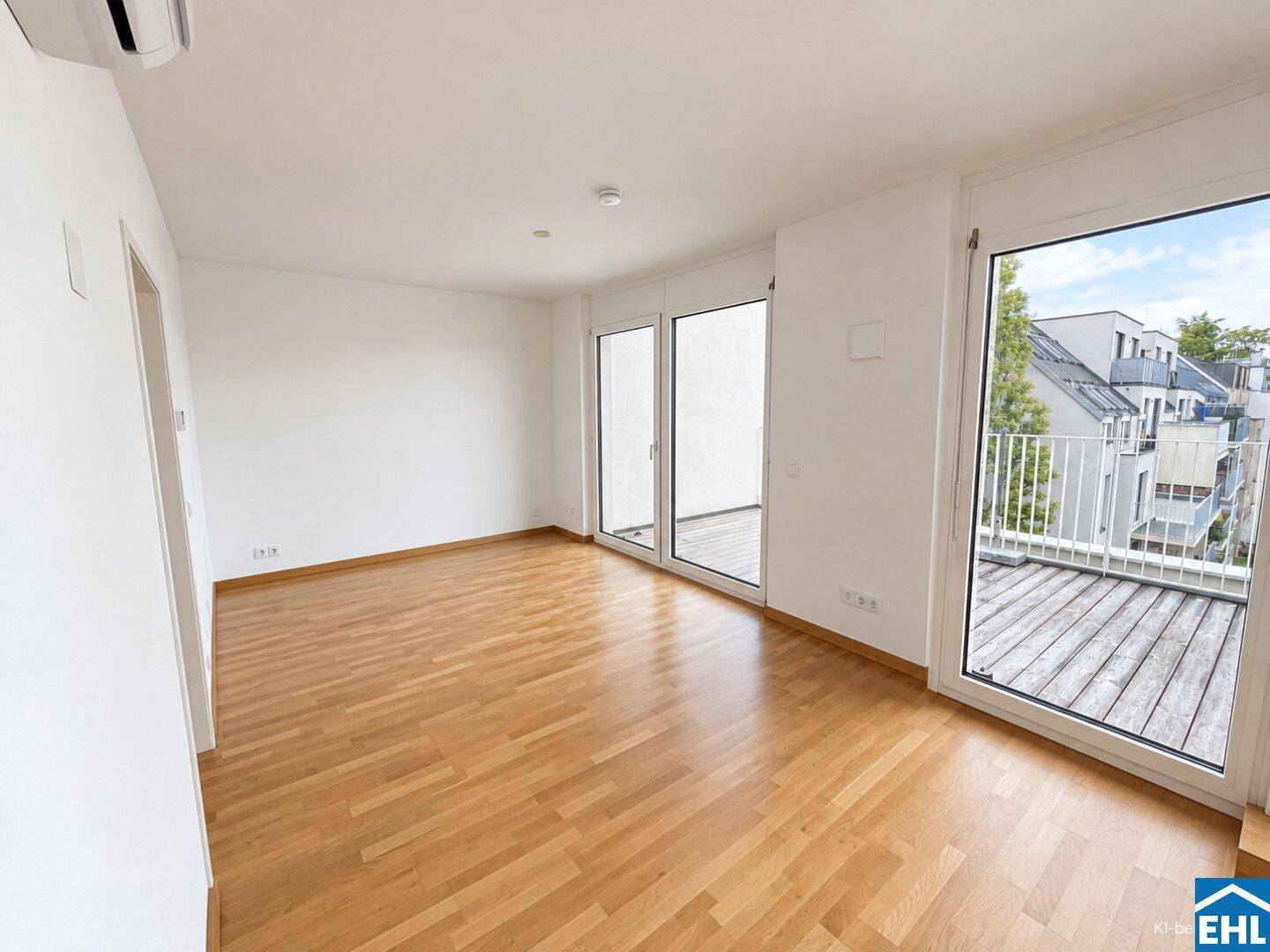 Helles, leeres Wohnzimmer mit Holzboden, weißen Wänden und Zugang zu einem Außenbereich.