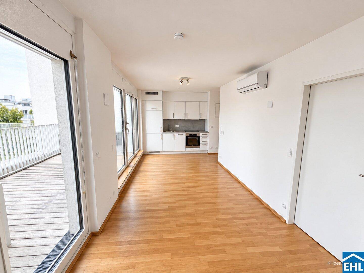Offener Wohnbereich mit integrierter Küchenzeile, Holzboden und großzügigem Zugang zur Terrasse.