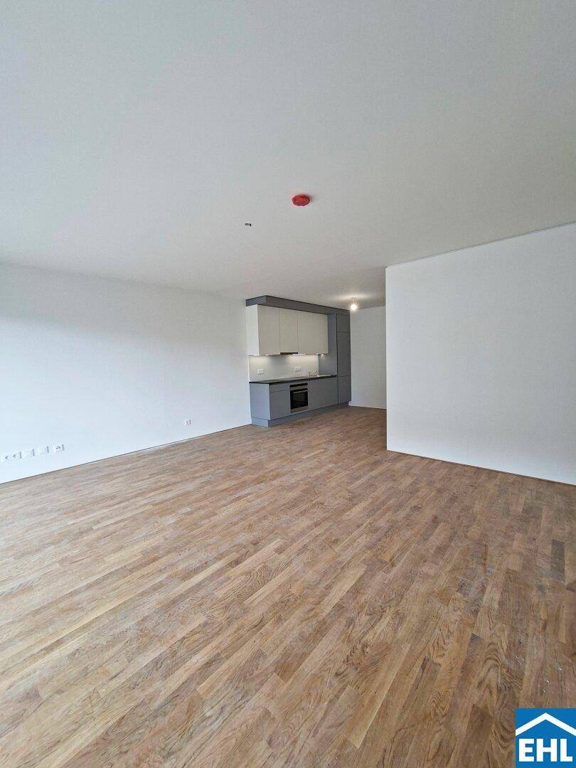 Geräumiger Wohnbereich mit Holzboden und moderner Küchenzeile in Grau- und Weißtönen.