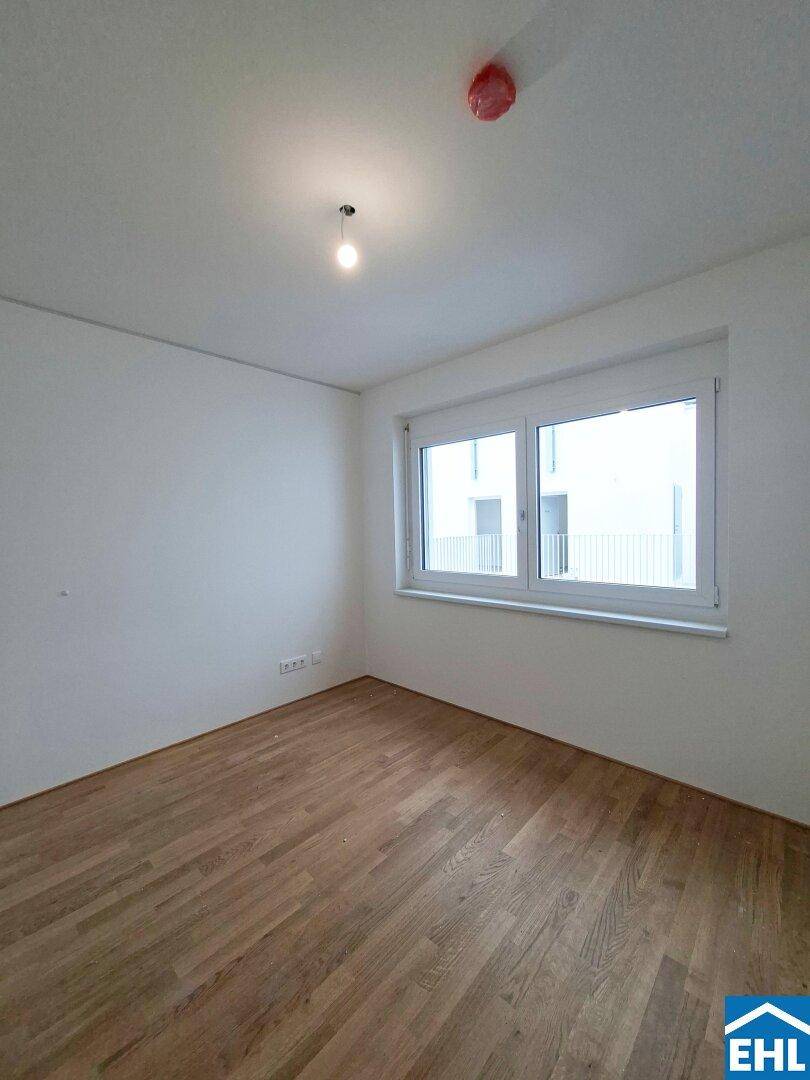 Ruhiges Schlafzimmer mit Parkettboden und einem Fenster, das viel Tageslicht hereinlässt.