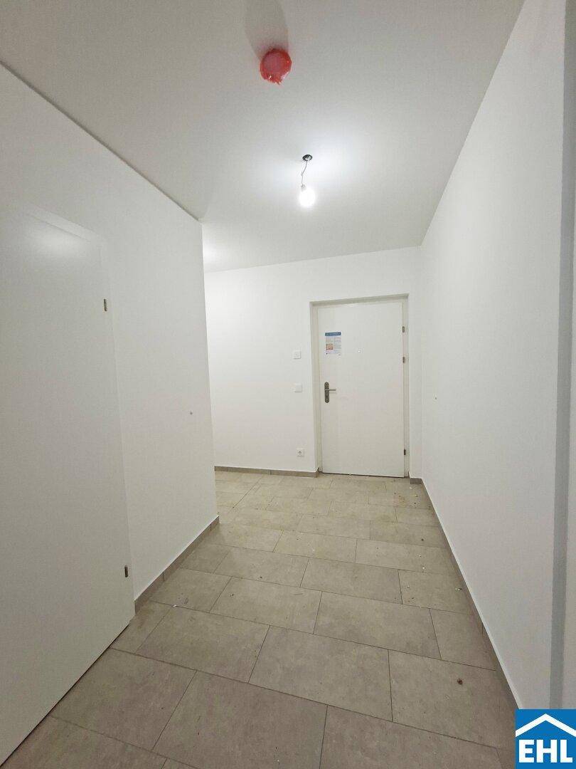 Heller Flur mit Fliesenboden und weiß gestrichenen Wänden, führt zu den Wohnräumen.
