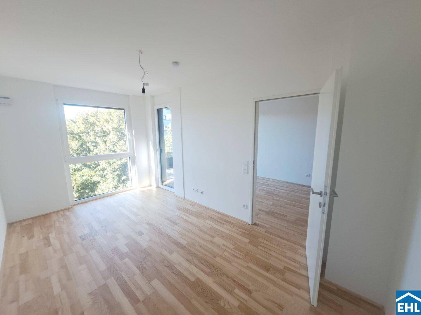Heller, leerer Raum mit Parkettboden und großen Fenstern, die viel Tageslicht hereinlassen.
