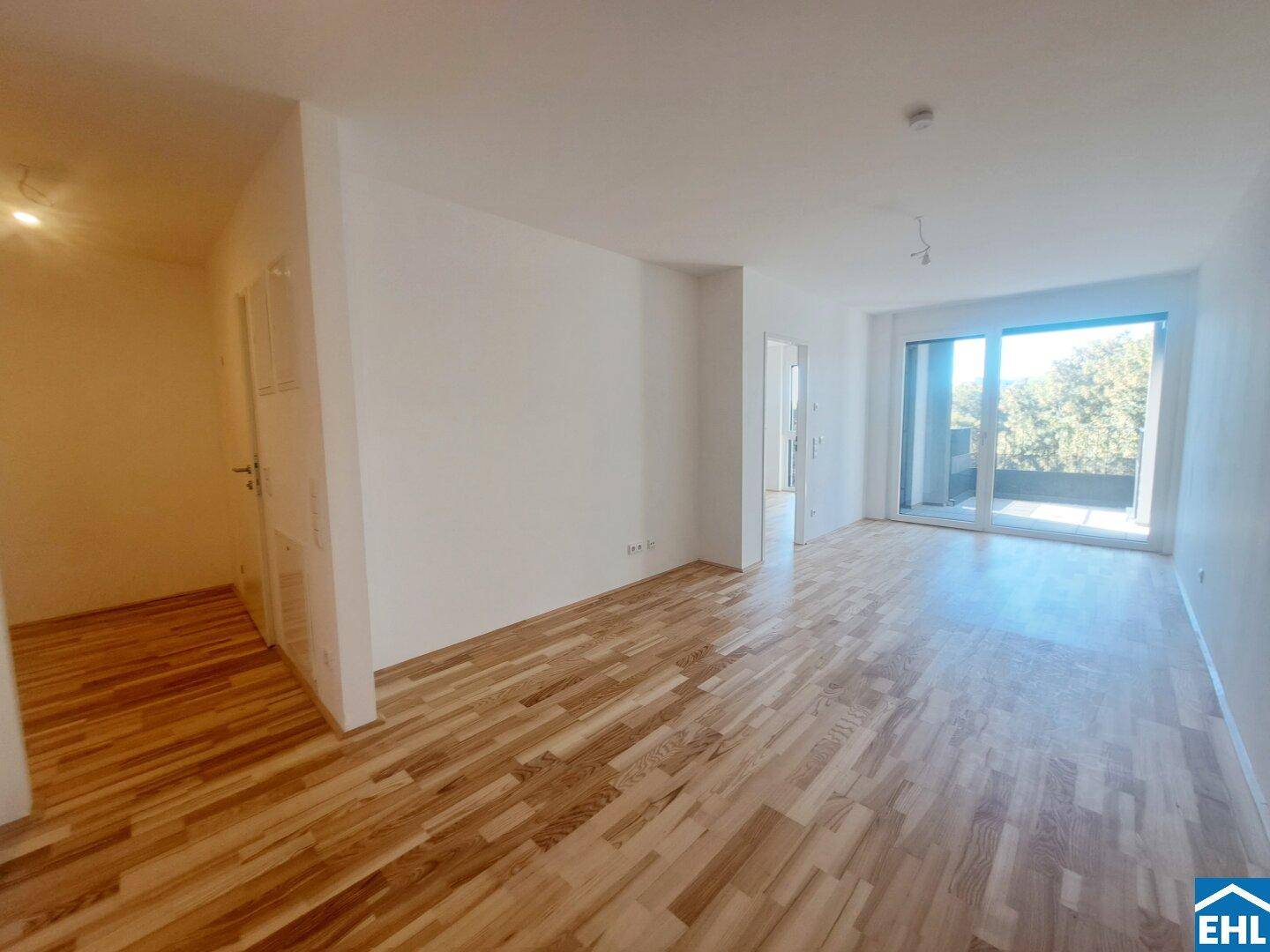 Geräumiger Wohnbereich mit Parkettboden und Zugang zu einem sonnigen Balkon.