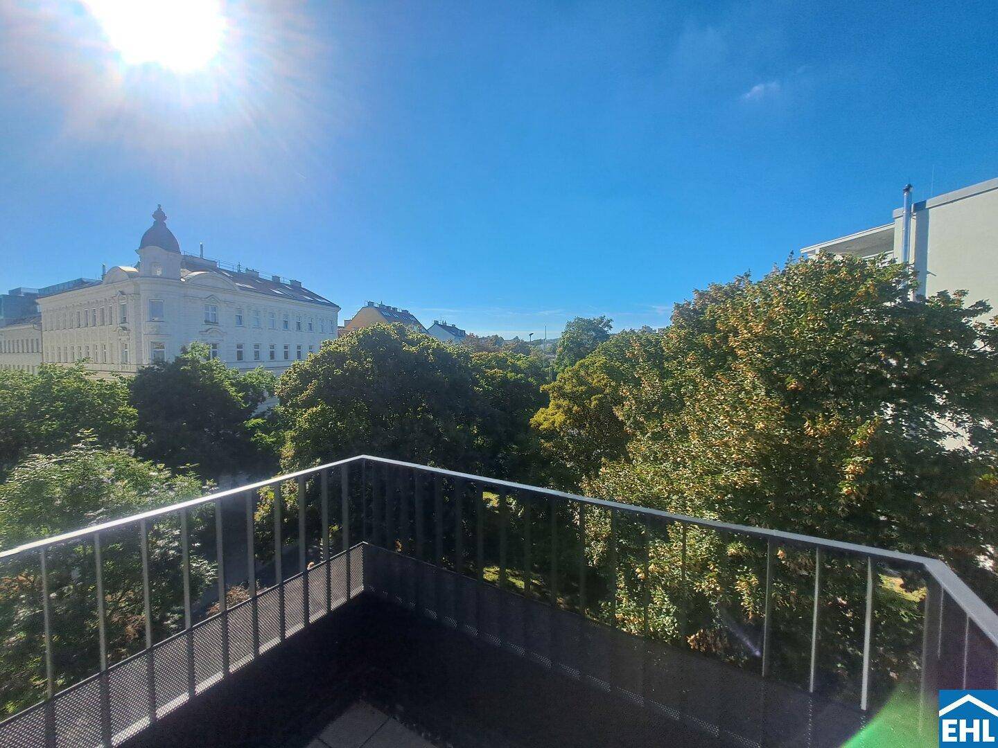 Sonniger Balkon mit weitem Blick über die Stadt und umliegende Grünflächen.
