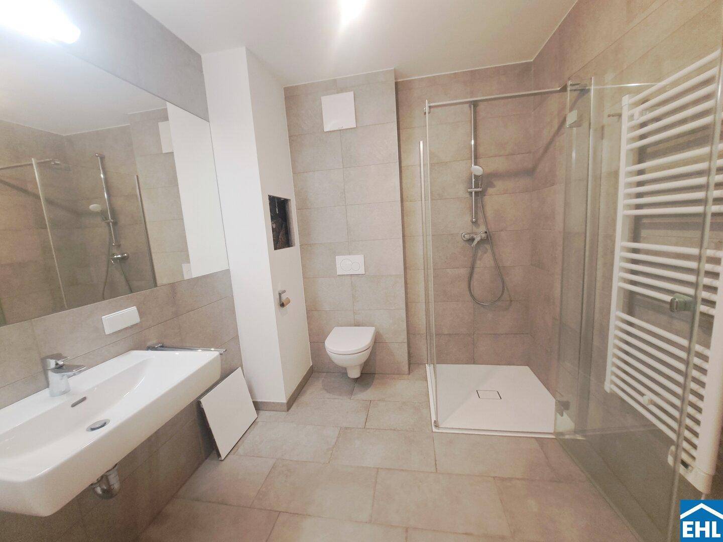 Helles Badezimmer mit großer Duschkabine, Wand-WC, modernem Waschbecken und Handtuchheizkörper.