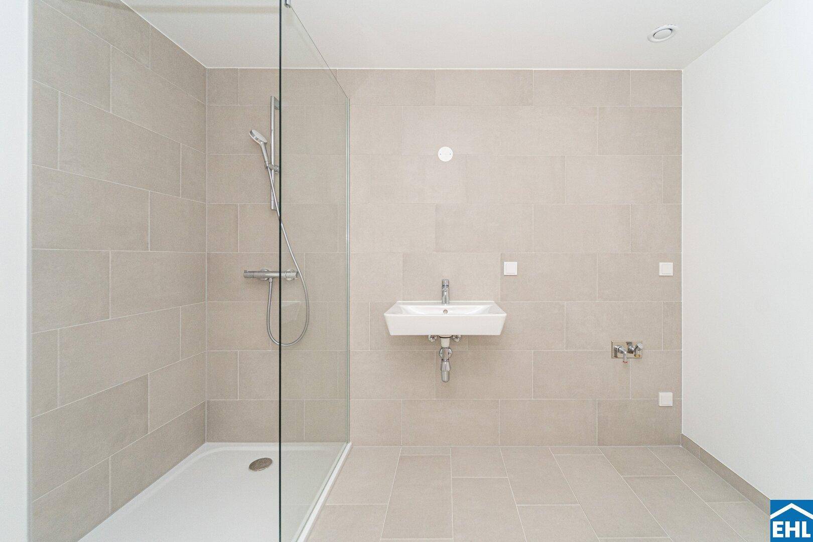 Modernes Badezimmer mit beigefarbenen Fliesen, ebenerdiger Dusche und Wandwaschbecken.