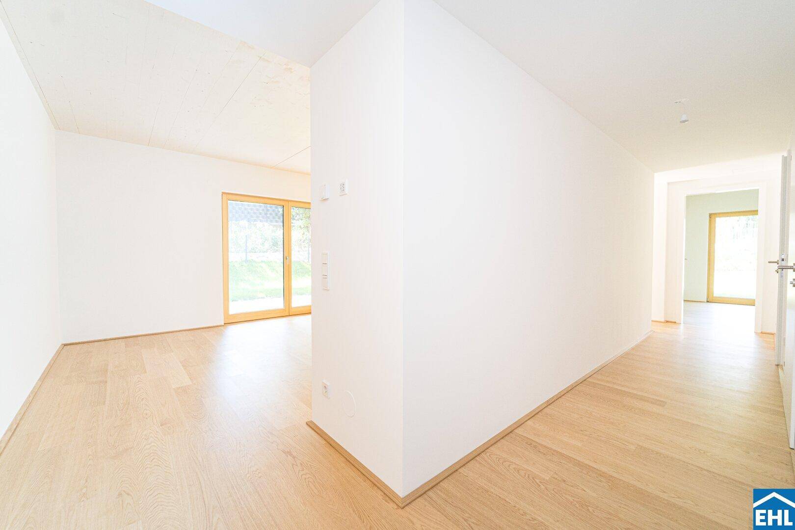 Heller Flur mit Holzboden, weißen Wänden und Blick in einen angrenzenden Raum.