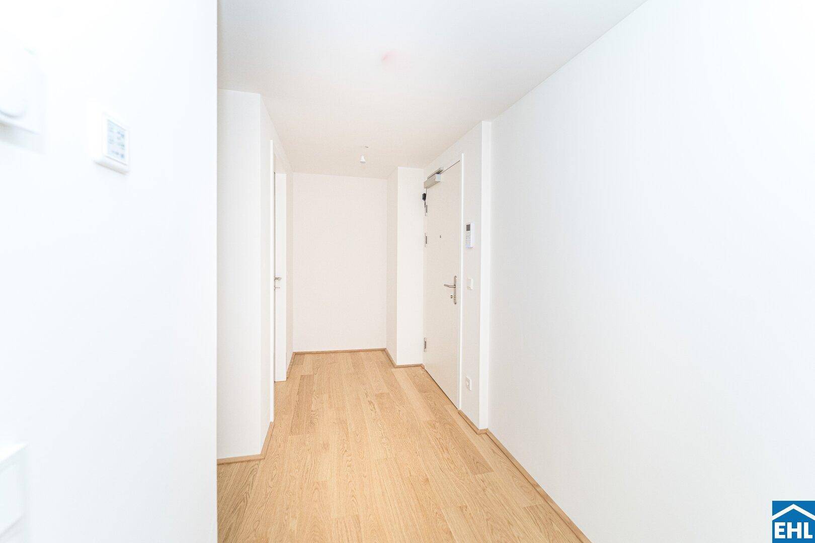 Eingangsflur mit hellem Holzboden, weißen Wänden und Gegensprechanlage.