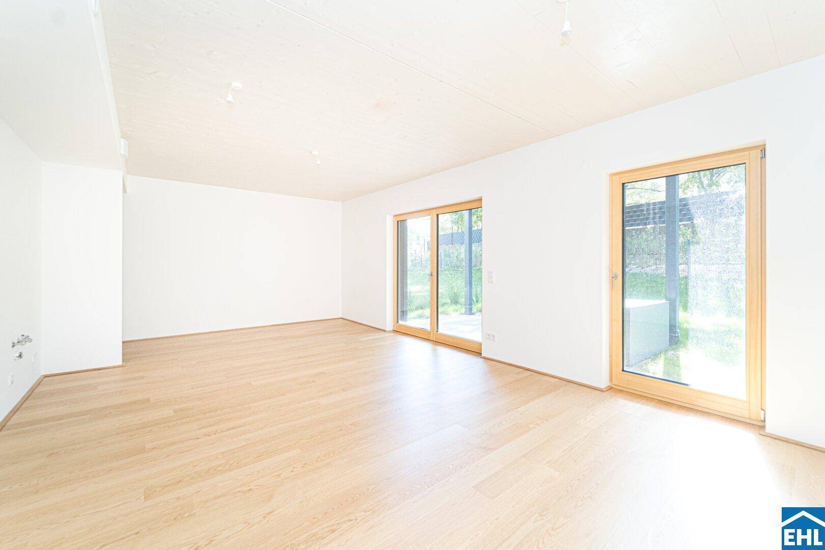 Heller, leerer Wohnraum mit Holzboden und großen Schiebetüren zum Garten.
