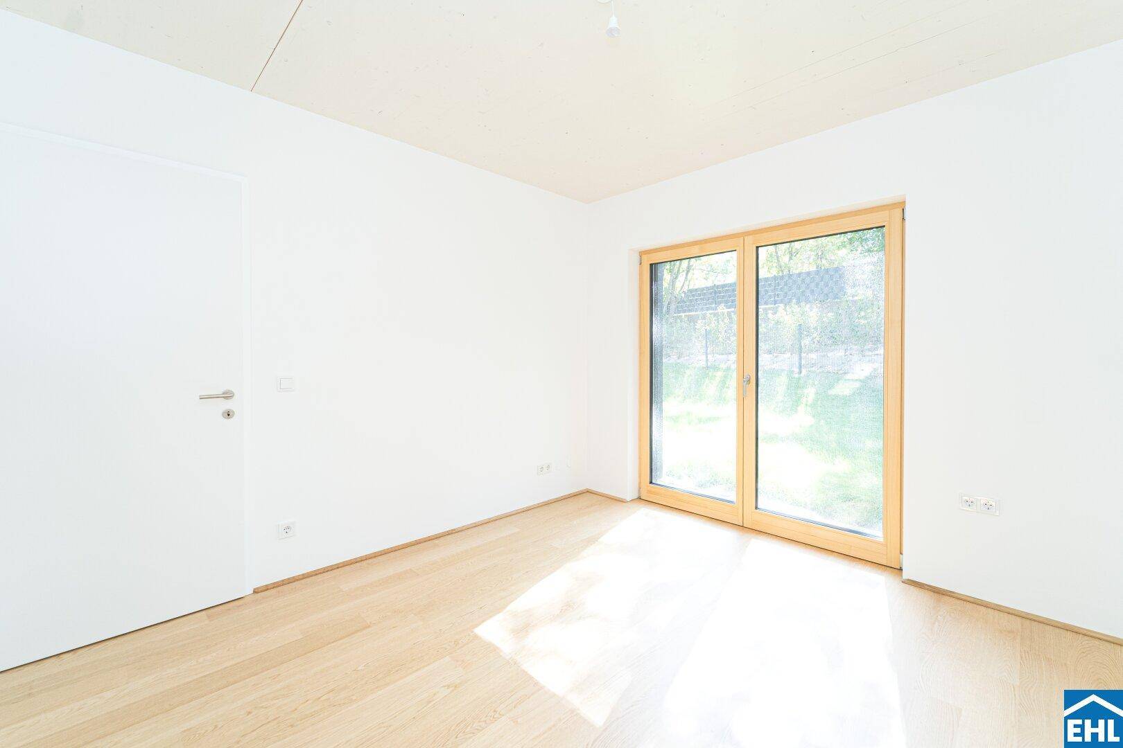 Helles Schlafzimmer mit Holzboden und Zugang zu einem Außenbereich durch eine Schiebetür.