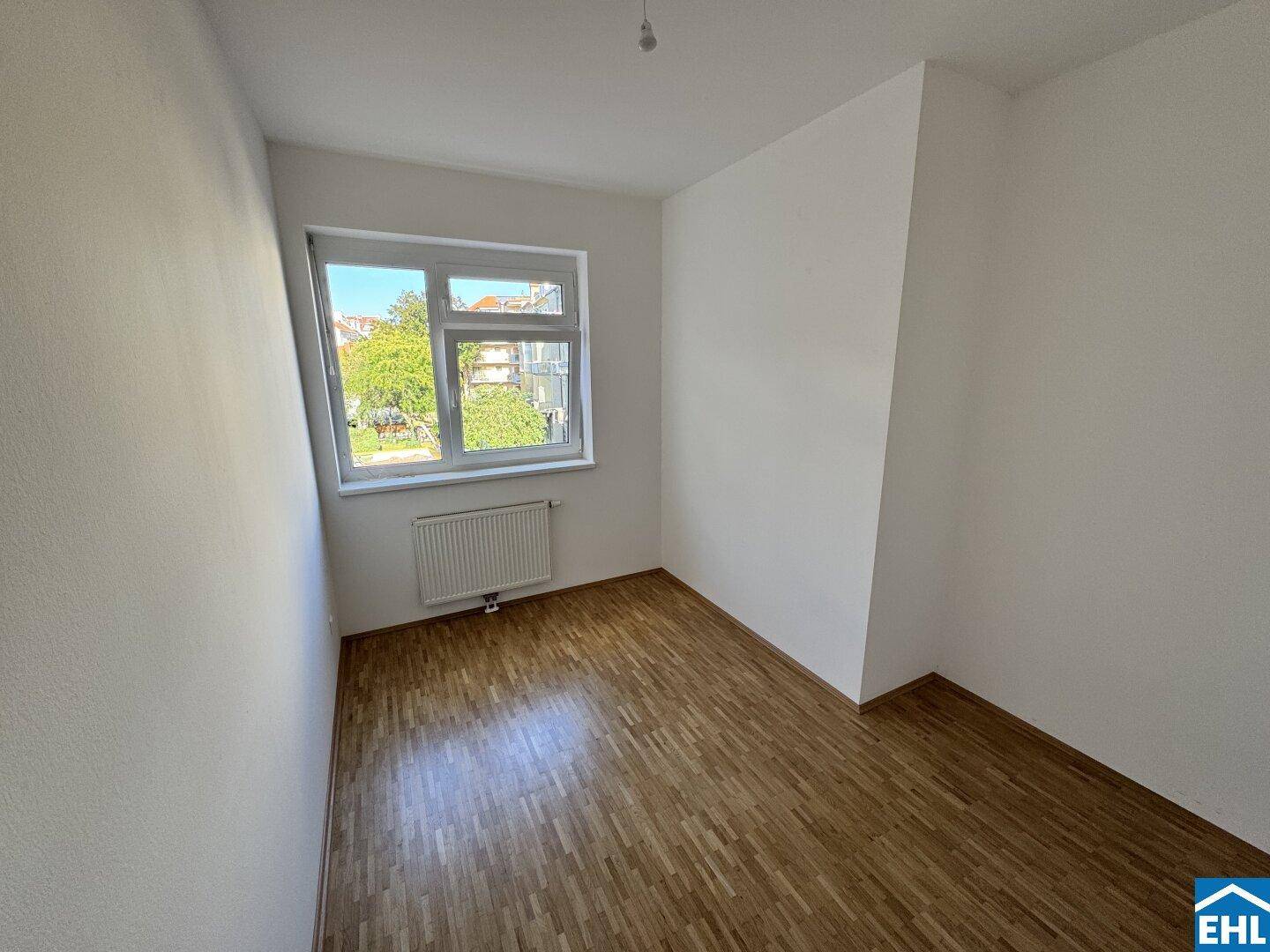 Freundliches Zimmer mit Parkettboden, großen Fenstern und viel natürlichem Lichteinfall.