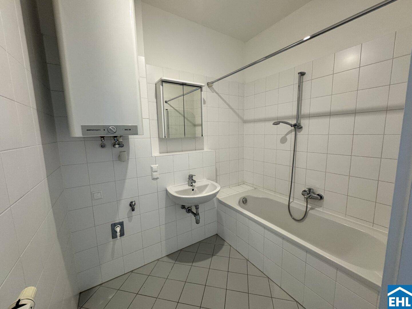 Funktionales Badezimmer mit Badewanne, Waschbecken, Wandspiegel und weißen Fliesen.
