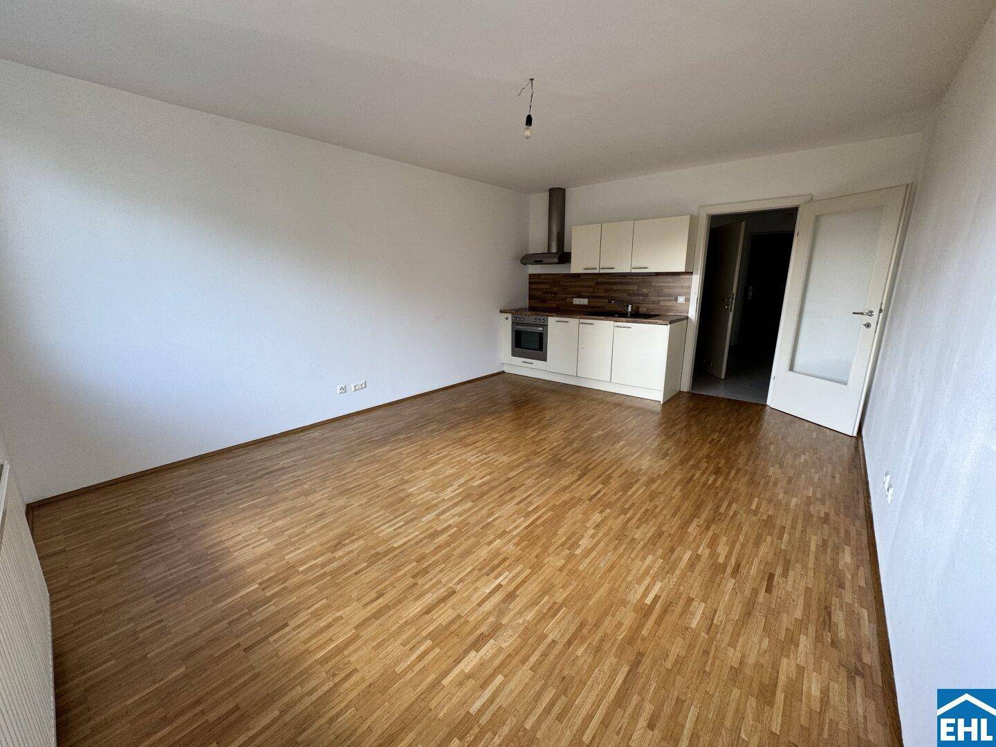 Geräumiger Wohnbereich mit integrierter Küchenzeile, Parkettboden und viel Tageslicht.