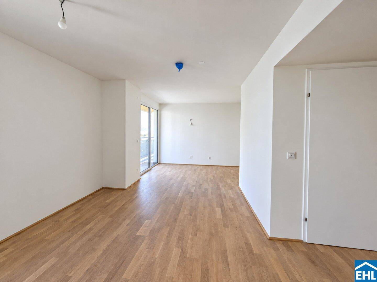 Geräumiger, unmöblierter Wohnbereich mit hellem Parkettboden und Schiebetür zum Außenbereich.