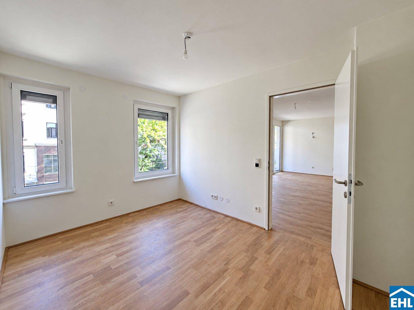 Unmöbliertes Zimmer mit Parkettboden und zwei Fenstern, die viel Licht spenden.