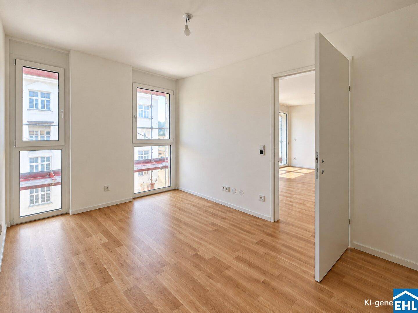 Leeres Zimmer mit Holzboden, großen Fenstern und Zugang zu weiteren Räumen.