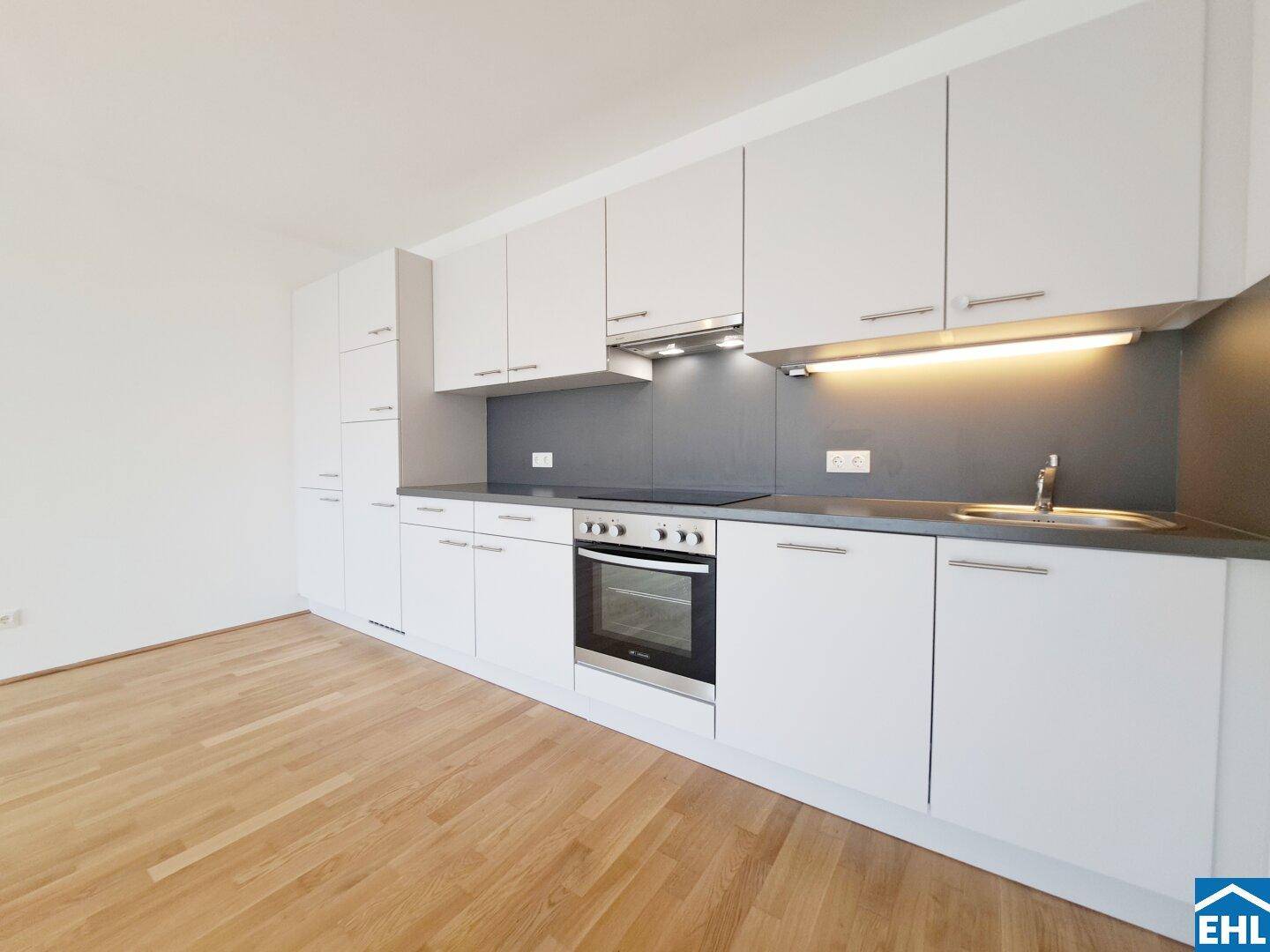 Moderne Einbauküche mit weißen Schränken, integrierten Geräten und dunkler Arbeitsplatte.