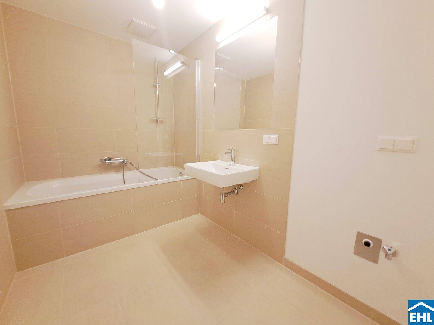 Modernes Badezimmer mit Badewanne, Waschbecken und beigefarbenen Fliesen, hell und funktional.
