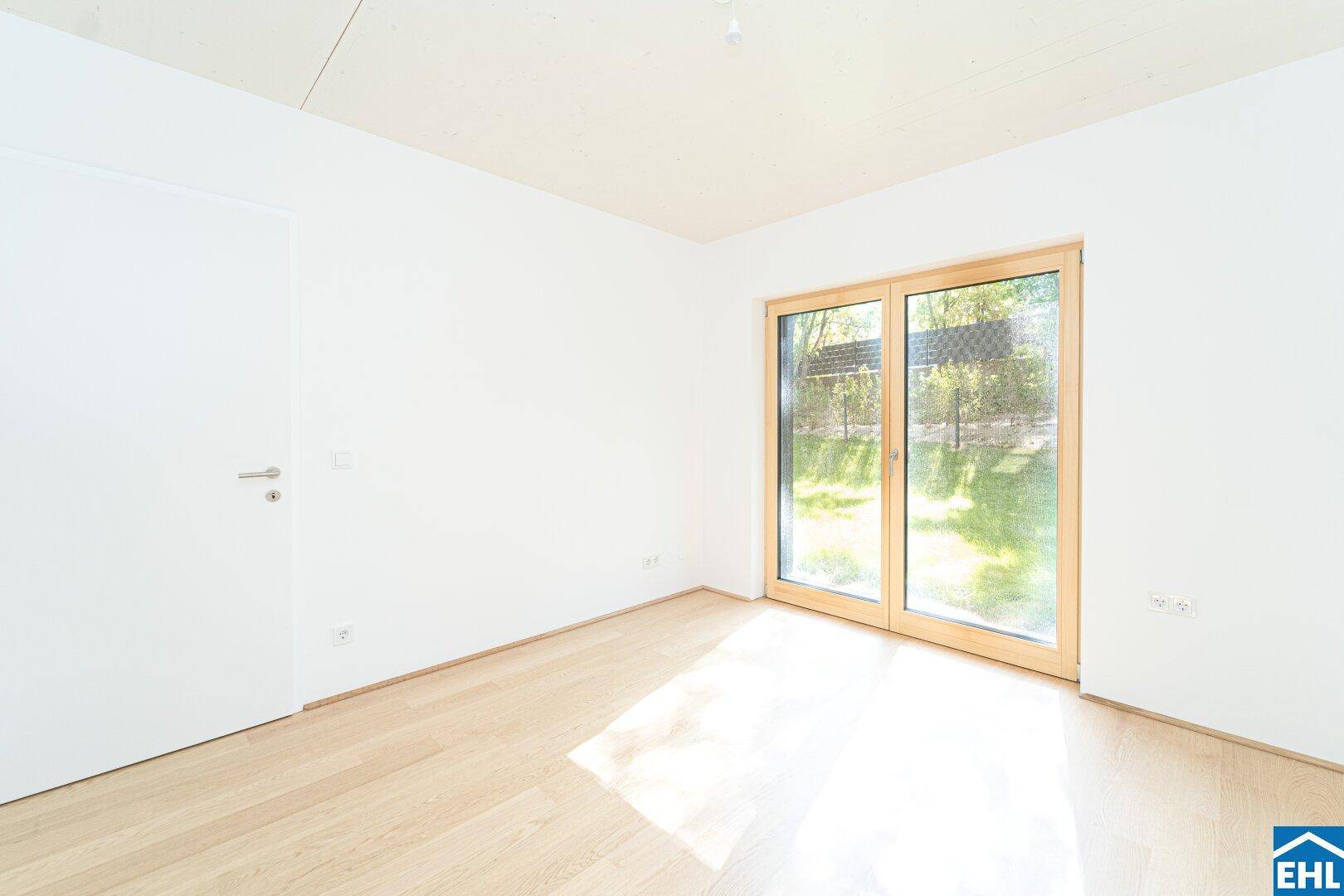 Helles Schlafzimmer mit Holzboden und Zugang zu einem Außenbereich durch eine große Glastür.