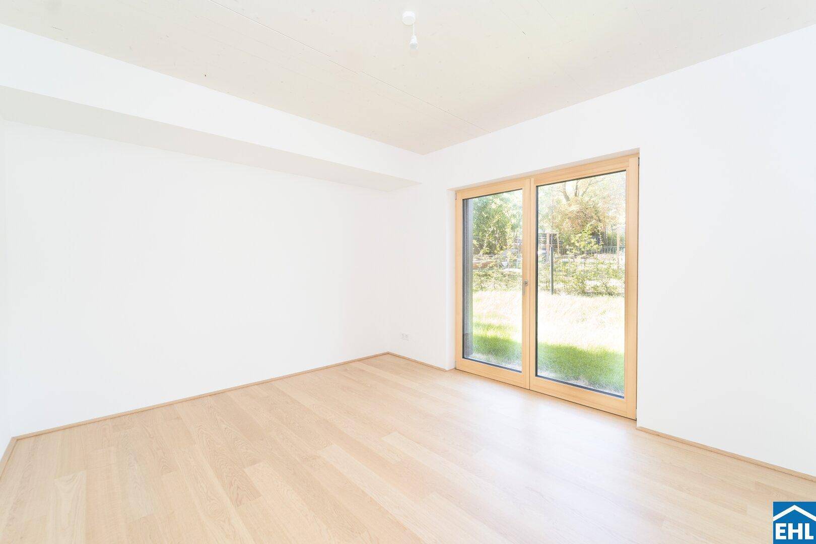 Lichtdurchflutetes Zimmer mit Holzboden und Blick ins Grüne durch eine breite Fenstertür.
