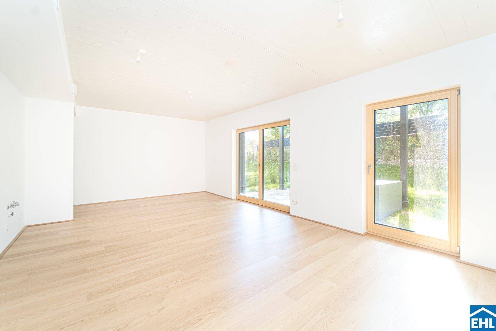 Helles, leeres Wohnzimmer mit Holzboden und großen Schiebetüren zum Gartenbereich.